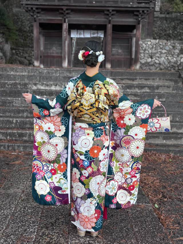 山門の石段の前で袖を広げる緑の振袖姿