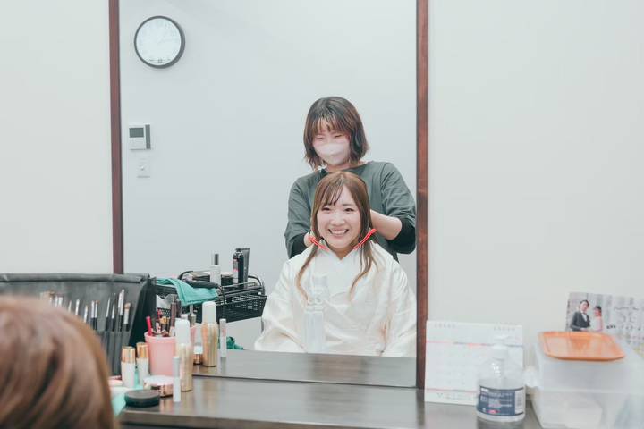 サロンの鏡越しに白無垢の花嫁のヘアをセットするスタッフ