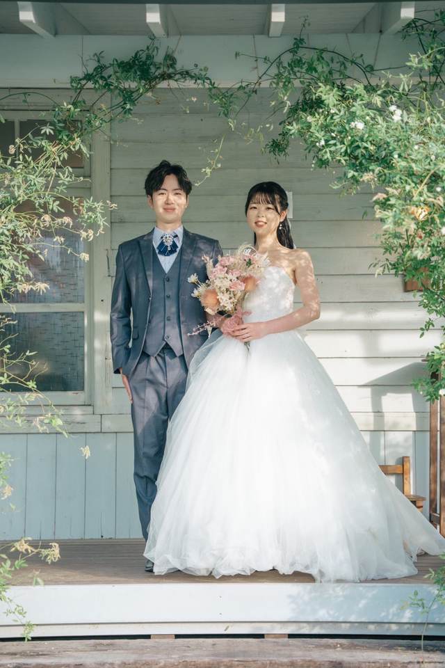 花に囲まれたポーチに並んで立つドレスとスーツの二人