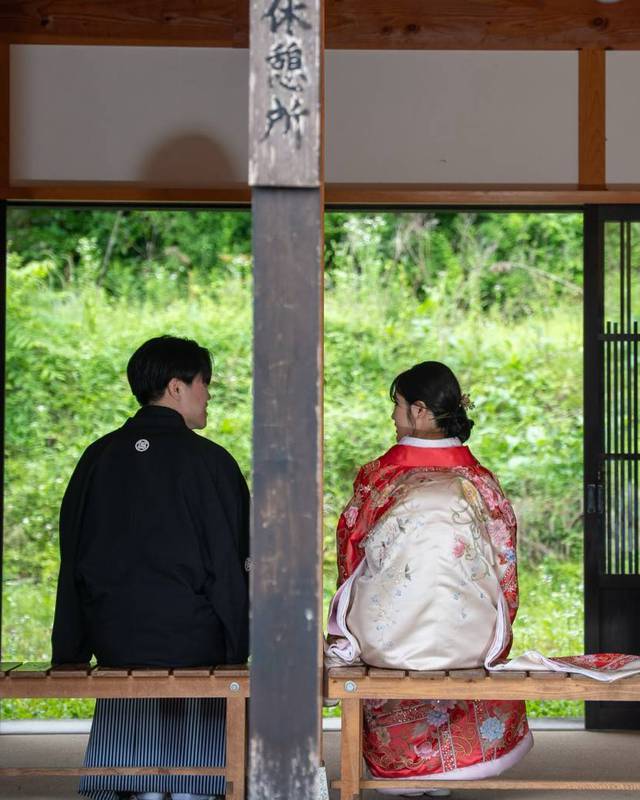 古民家の縁側に並んで腰かける色打掛と黒紋付の二人